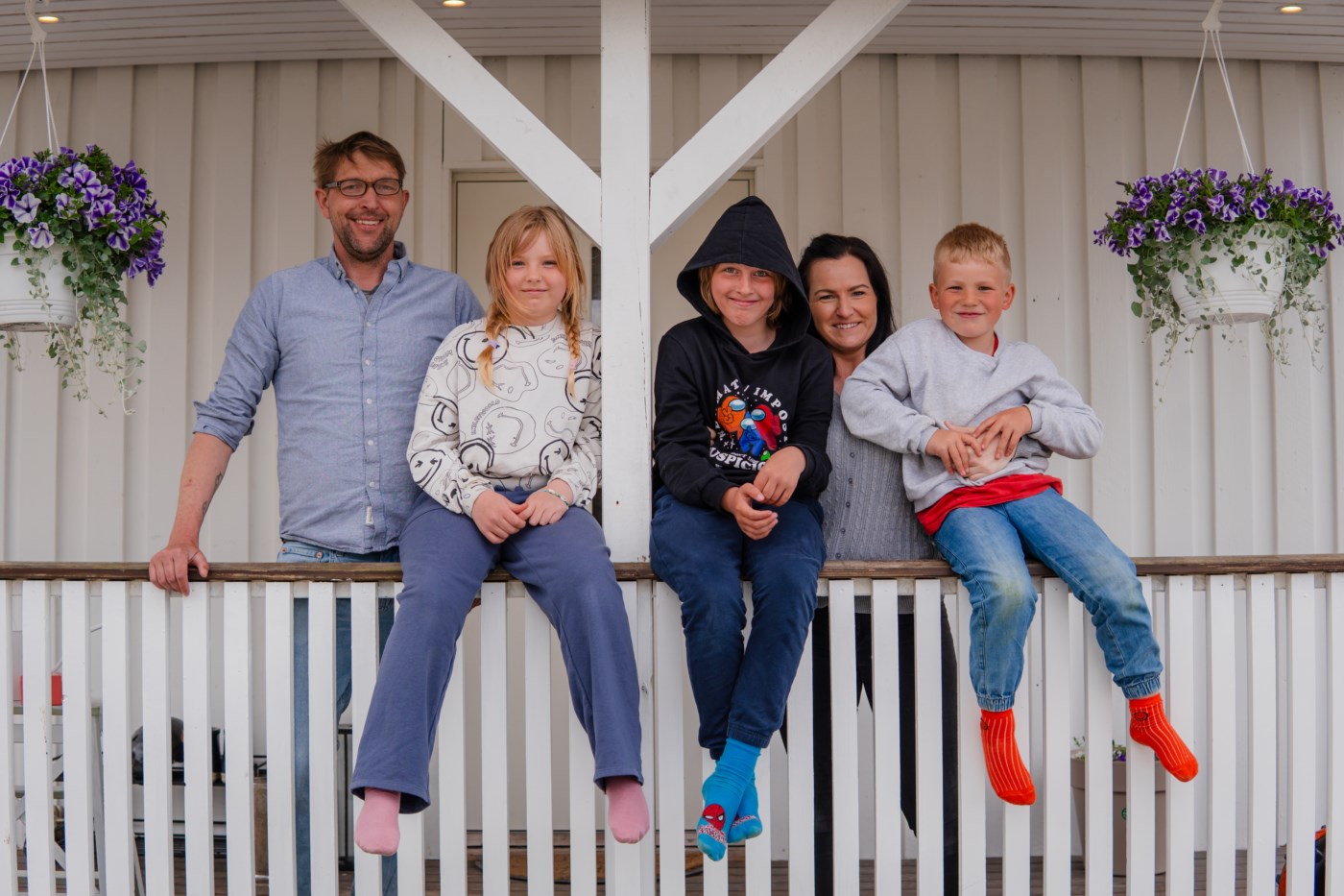 Familie med mor, far, to sønner og en datter står foran en trevegg.