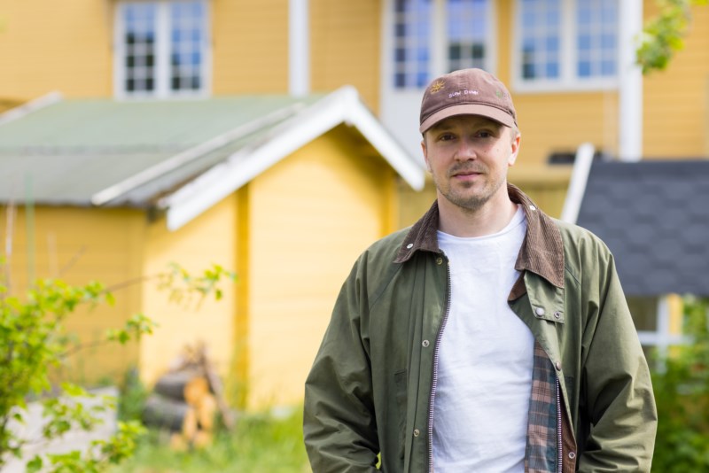 Portrett av en mann med caps foran et gult hus.