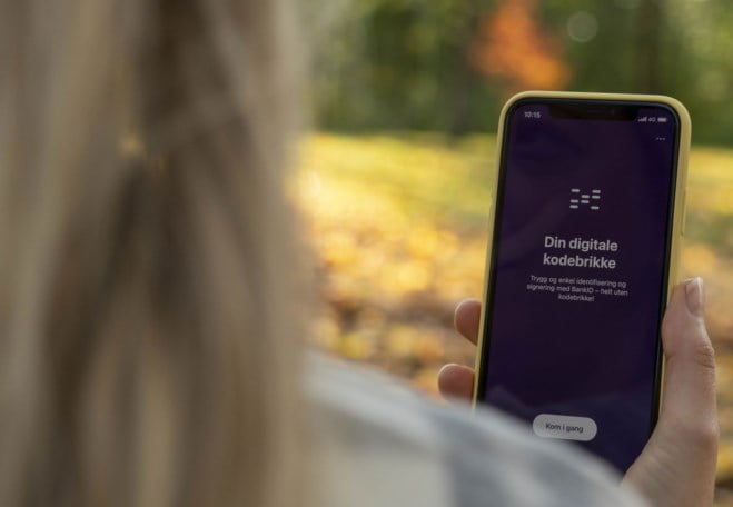 Kvinne med langt, blondt hår holder mobil med BankID-appen synlig